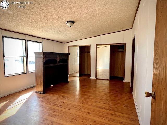 unfurnished living room featuring light wood-style flooring, a textured ceiling, baseboards, and crown molding