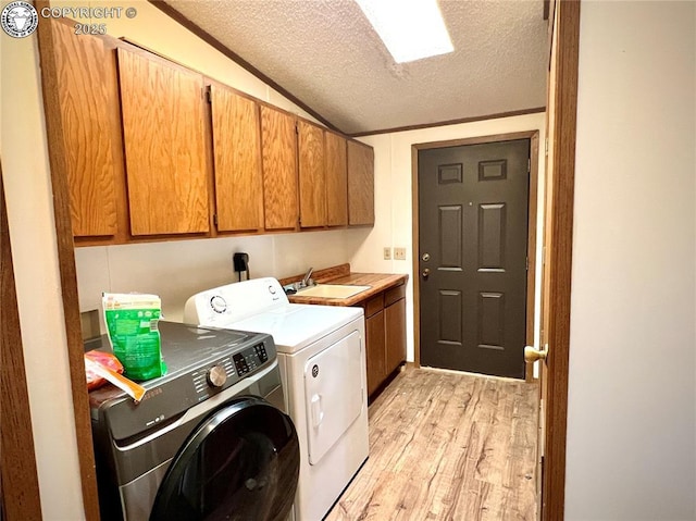 laundry area with a textured ceiling, a sink, washer and dryer, light wood-type flooring, and cabinet space