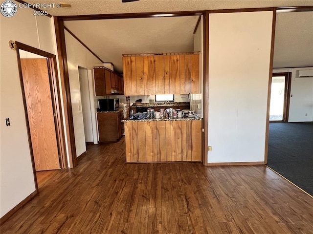 kitchen with dark wood-style flooring, dark stone countertops, and brown cabinets