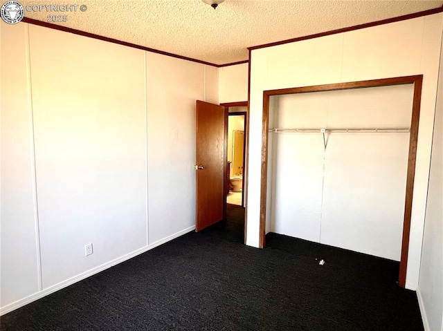 unfurnished bedroom featuring dark colored carpet, a closet, a decorative wall, ornamental molding, and a textured ceiling