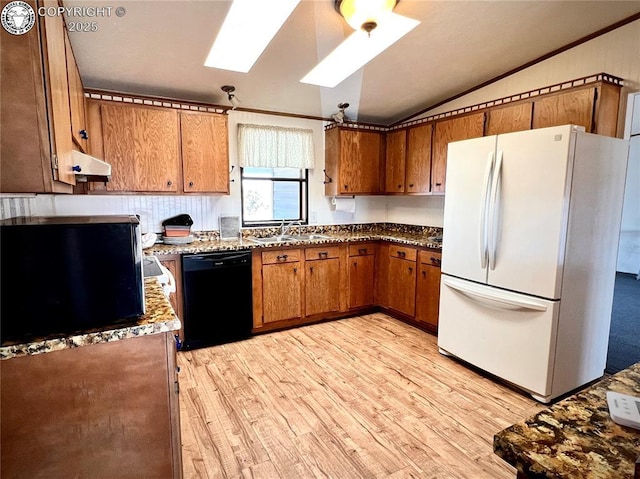 kitchen featuring brown cabinets, light wood-style flooring, freestanding refrigerator, vaulted ceiling with skylight, and dishwasher