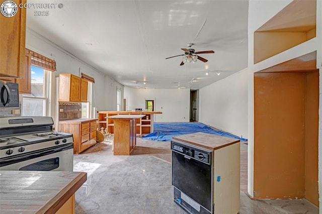 122 W Main St, Florence, CO 81226 - kitchen featuring stainless steel range with gas cooktop, black microwave, ceiling fan, a center island, and brown cabinetry