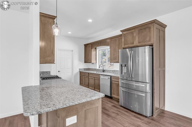 kitchen with pendant lighting, sink, stainless steel appliances, light hardwood / wood-style floors, and kitchen peninsula