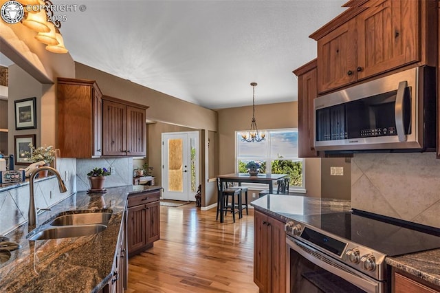 kitchen featuring sink, appliances with stainless steel finishes, dark stone countertops, backsplash, and hanging light fixtures