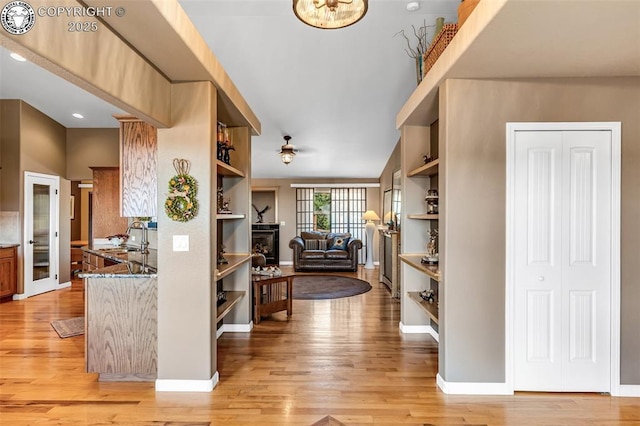 kitchen with sink, built in features, ceiling fan, dark stone countertops, and light wood-type flooring