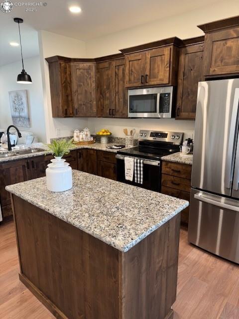 kitchen with appliances with stainless steel finishes, dark brown cabinetry, light stone countertops, decorative light fixtures, and sink