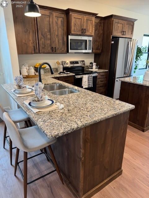 kitchen featuring appliances with stainless steel finishes, hanging light fixtures, light stone countertops, light hardwood / wood-style floors, and sink