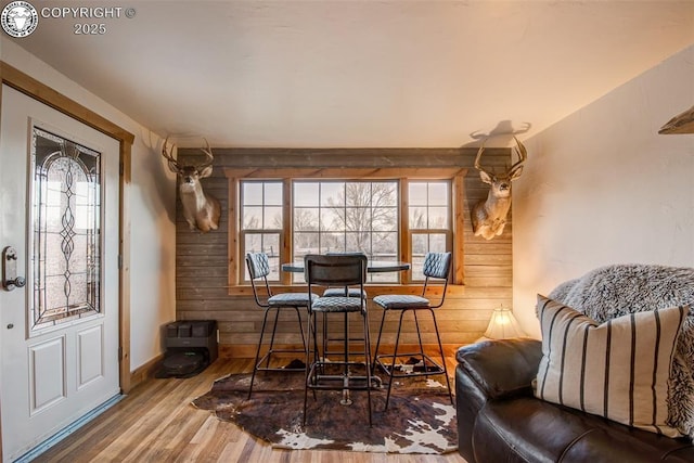 dining space featuring baseboards, wood walls, wood finished floors, and a healthy amount of sunlight