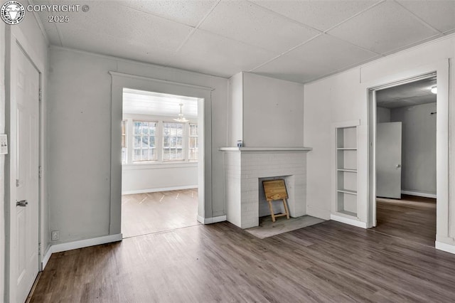 unfurnished living room featuring a paneled ceiling, baseboards, and wood finished floors