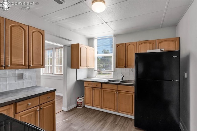 kitchen featuring a sink, light wood-type flooring, freestanding refrigerator, brown cabinets, and decorative backsplash