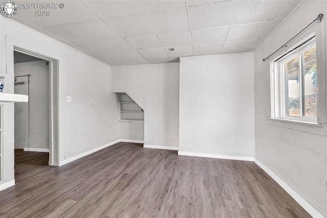 basement with a paneled ceiling, wood finished floors, and baseboards