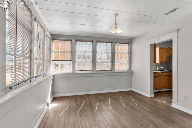 unfurnished dining area featuring a sink, visible vents, baseboards, and wood finished floors