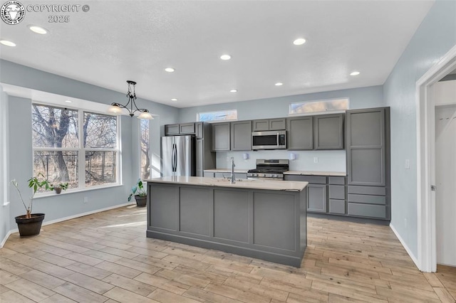 kitchen with gray cabinets, light countertops, appliances with stainless steel finishes, a sink, and an island with sink