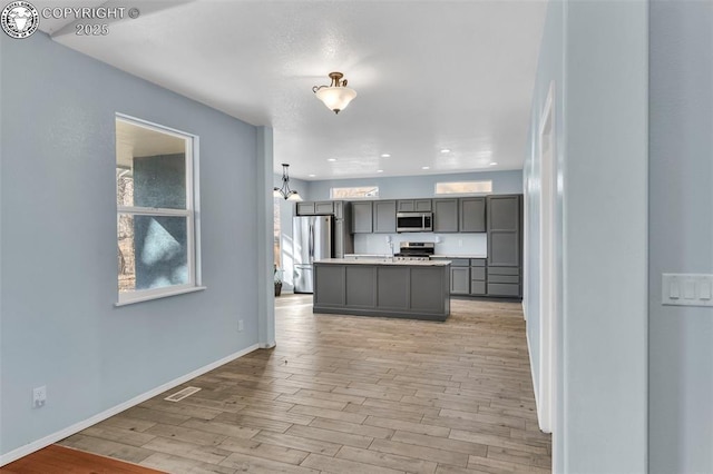 kitchen featuring light wood-style flooring, light countertops, appliances with stainless steel finishes, gray cabinets, and a center island