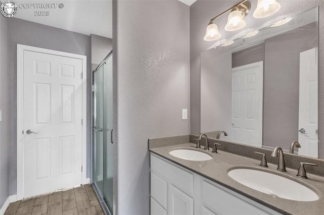 full bathroom with double vanity, a shower with door, a sink, and wood finished floors