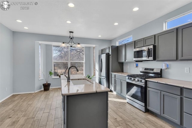 kitchen with pendant lighting, stainless steel appliances, gray cabinets, a sink, and an island with sink