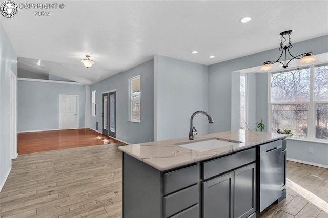 kitchen featuring hanging light fixtures, stainless steel dishwasher, a kitchen island with sink, a sink, and light stone countertops