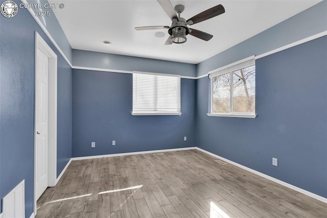 spare room featuring light wood-style flooring, a ceiling fan, visible vents, and baseboards