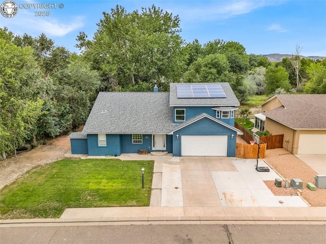 traditional home featuring a garage, a shingled roof, fence, roof mounted solar panels, and a front lawn