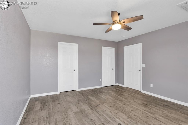 unfurnished bedroom with ceiling fan, wood finished floors, two closets, and baseboards