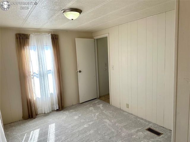 unfurnished bedroom featuring wooden walls, carpet floors, and visible vents