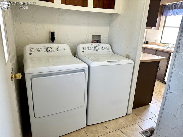 laundry room featuring a sink, light tile patterned floors, laundry area, visible vents, and independent washer and dryer