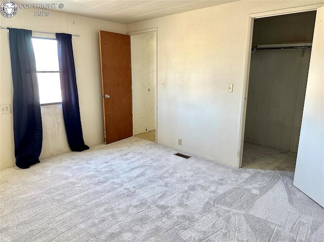 unfurnished bedroom with a walk in closet, a closet, visible vents, and carpet flooring