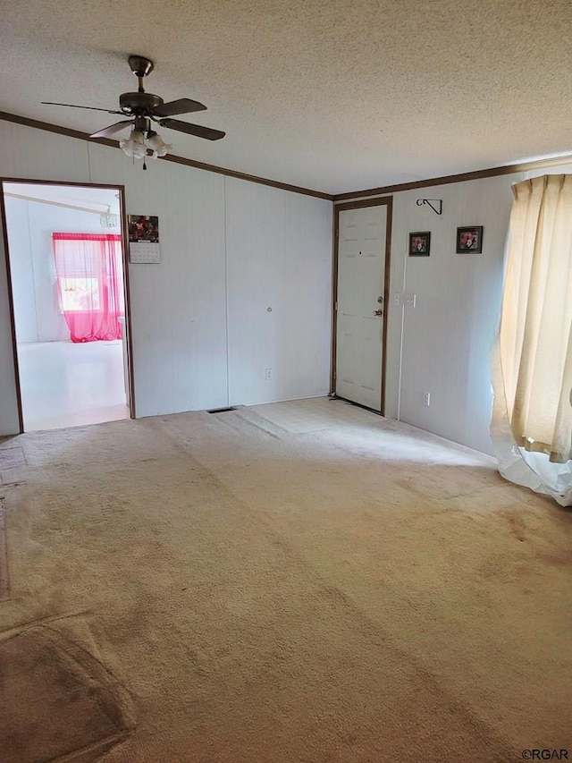 carpeted spare room featuring ceiling fan, ornamental molding, and a textured ceiling