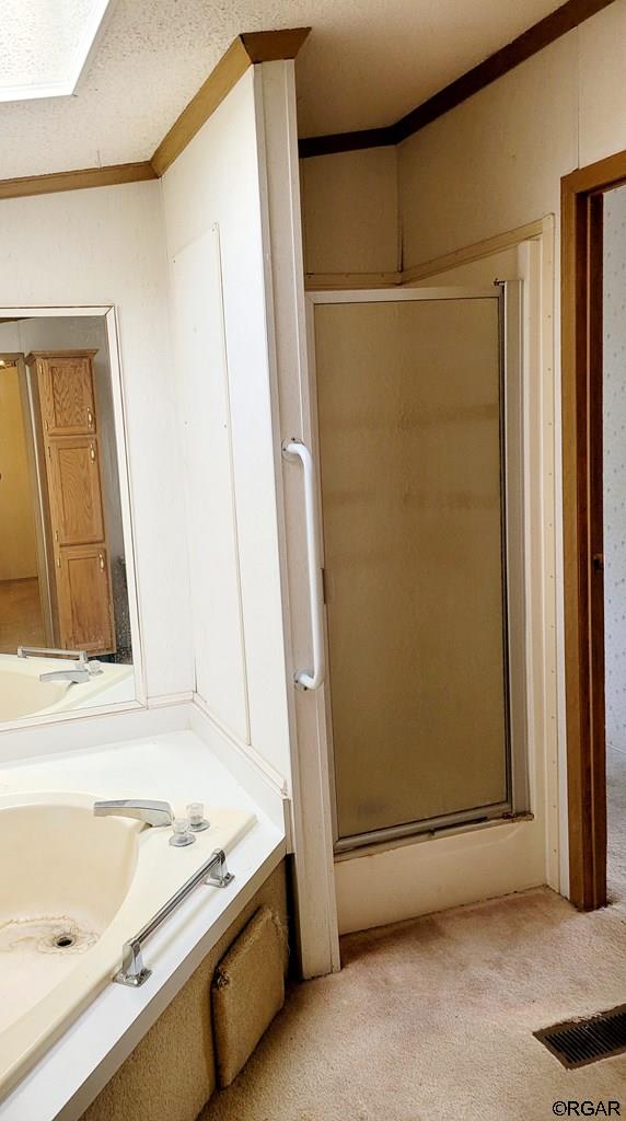 bathroom featuring shower with separate bathtub, ornamental molding, a textured ceiling, and a skylight