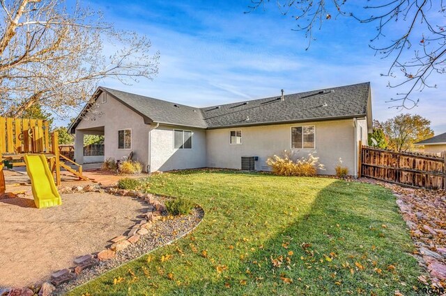 rear view of property featuring a playground, central air condition unit, and a lawn