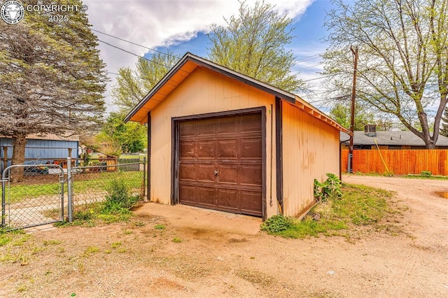 detached garage featuring fence, dirt driveway, and a gate