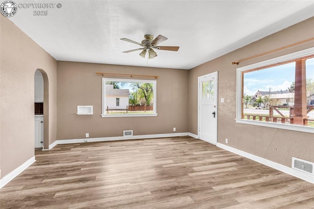 empty room featuring arched walkways, a ceiling fan, wood finished floors, and baseboards
