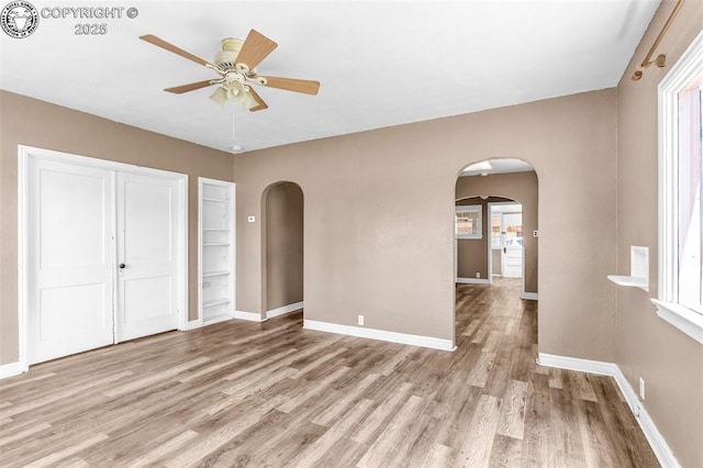 unfurnished bedroom featuring arched walkways, light wood-style floors, baseboards, and a closet