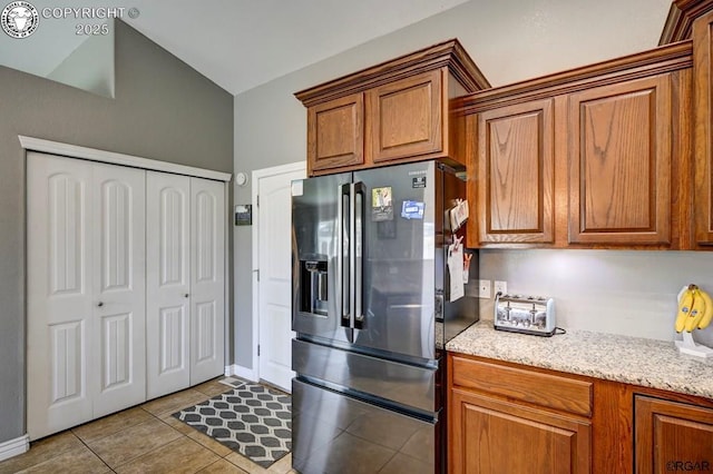 kitchen featuring brown cabinetry, tile patterned flooring, stainless steel fridge, and light stone countertops