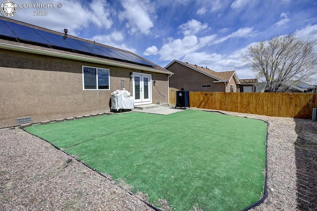 rear view of house featuring french doors, roof mounted solar panels, a fenced backyard, and stucco siding