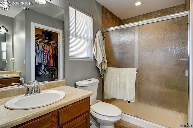 full bath featuring toilet, a spacious closet, a stall shower, and vanity