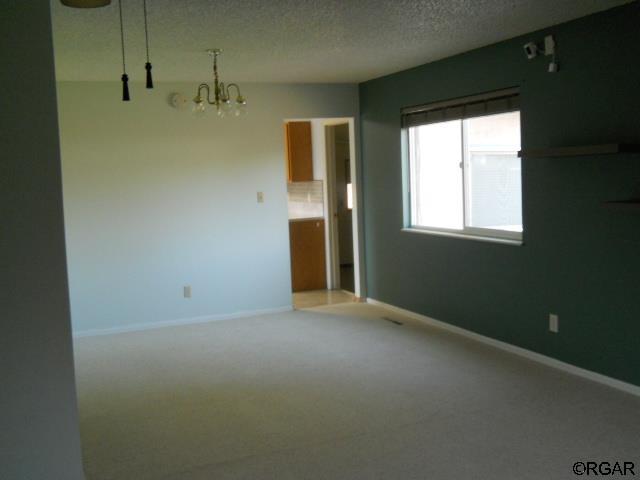 empty room with carpet flooring, a textured ceiling, and an inviting chandelier