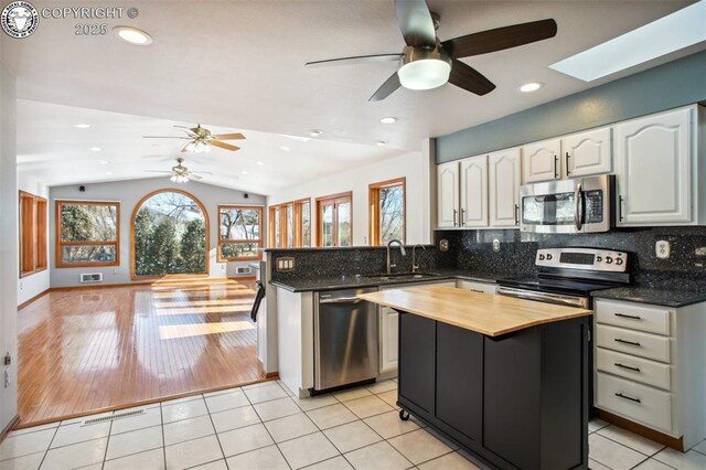 kitchen featuring sink, light tile patterned floors, appliances with stainless steel finishes, lofted ceiling with skylight, and kitchen peninsula