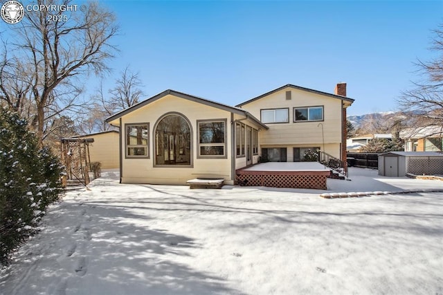 snow covered rear of property with a shed and a wooden deck