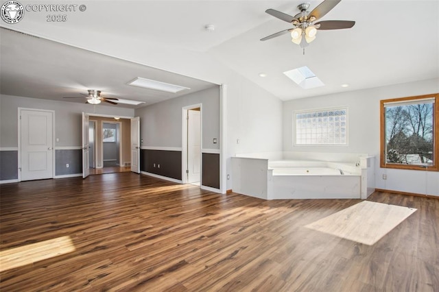 unfurnished living room featuring dark hardwood / wood-style floors, vaulted ceiling with skylight, and ceiling fan