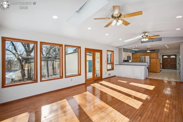 unfurnished living room featuring lofted ceiling with skylight and light wood-type flooring