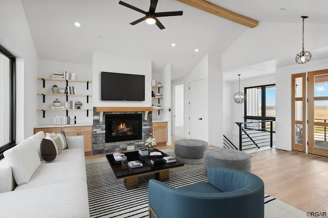 living room with a stone fireplace, high vaulted ceiling, light wood-type flooring, beamed ceiling, and ceiling fan with notable chandelier