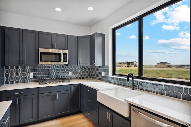 kitchen with sink, appliances with stainless steel finishes, tasteful backsplash, light stone counters, and light wood-type flooring