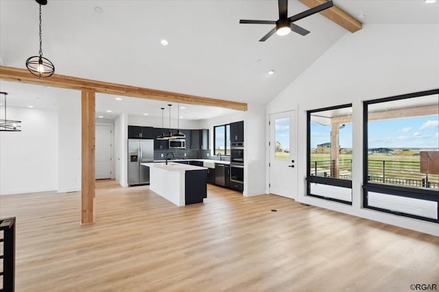 kitchen with pendant lighting, appliances with stainless steel finishes, tasteful backsplash, light hardwood / wood-style floors, and a center island with sink