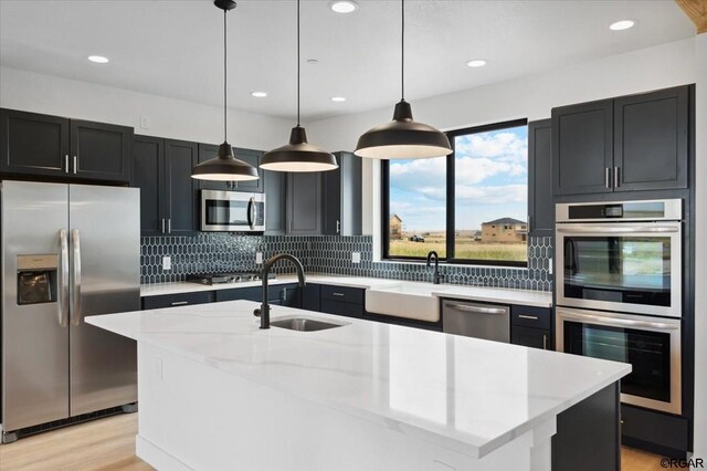 kitchen featuring sink, appliances with stainless steel finishes, light stone counters, an island with sink, and decorative light fixtures