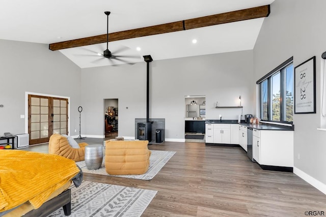 living room featuring hardwood / wood-style floors, a wood stove, ceiling fan, beam ceiling, and french doors