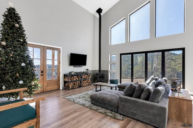 living room featuring a high ceiling, wood-type flooring, a wood stove, and french doors