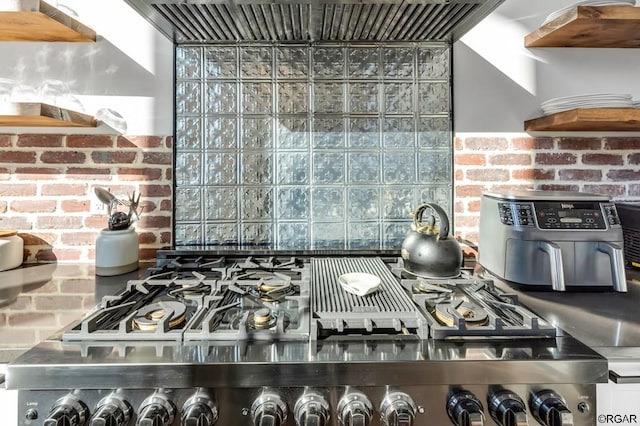 kitchen with extractor fan, brick wall, and stainless steel range