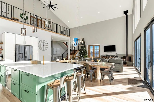 kitchen with high vaulted ceiling, a wood stove, white cabinets, stainless steel fridge, and green cabinets