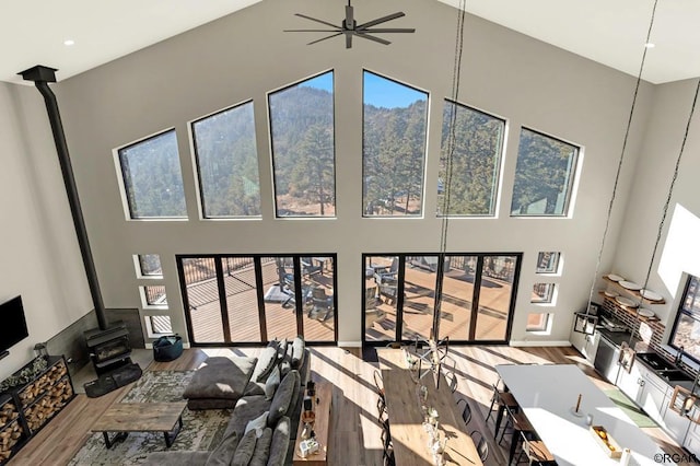 living room featuring hardwood / wood-style floors, a high ceiling, ceiling fan, and a wood stove